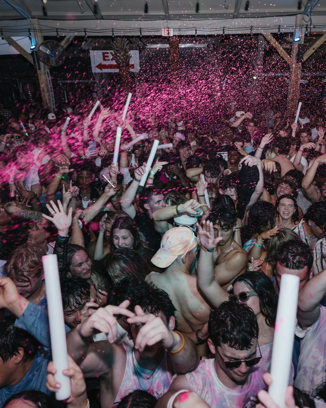 A packed spring break party crowd waving glow sticks under pink confetti in Panama City Beach