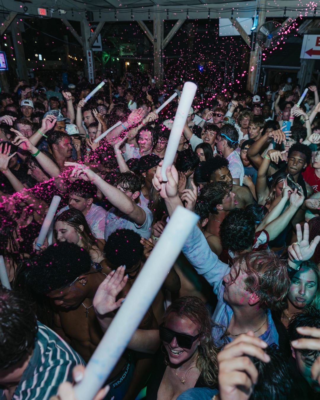 A group of friends in a crowd under pink confetti and glow sticks