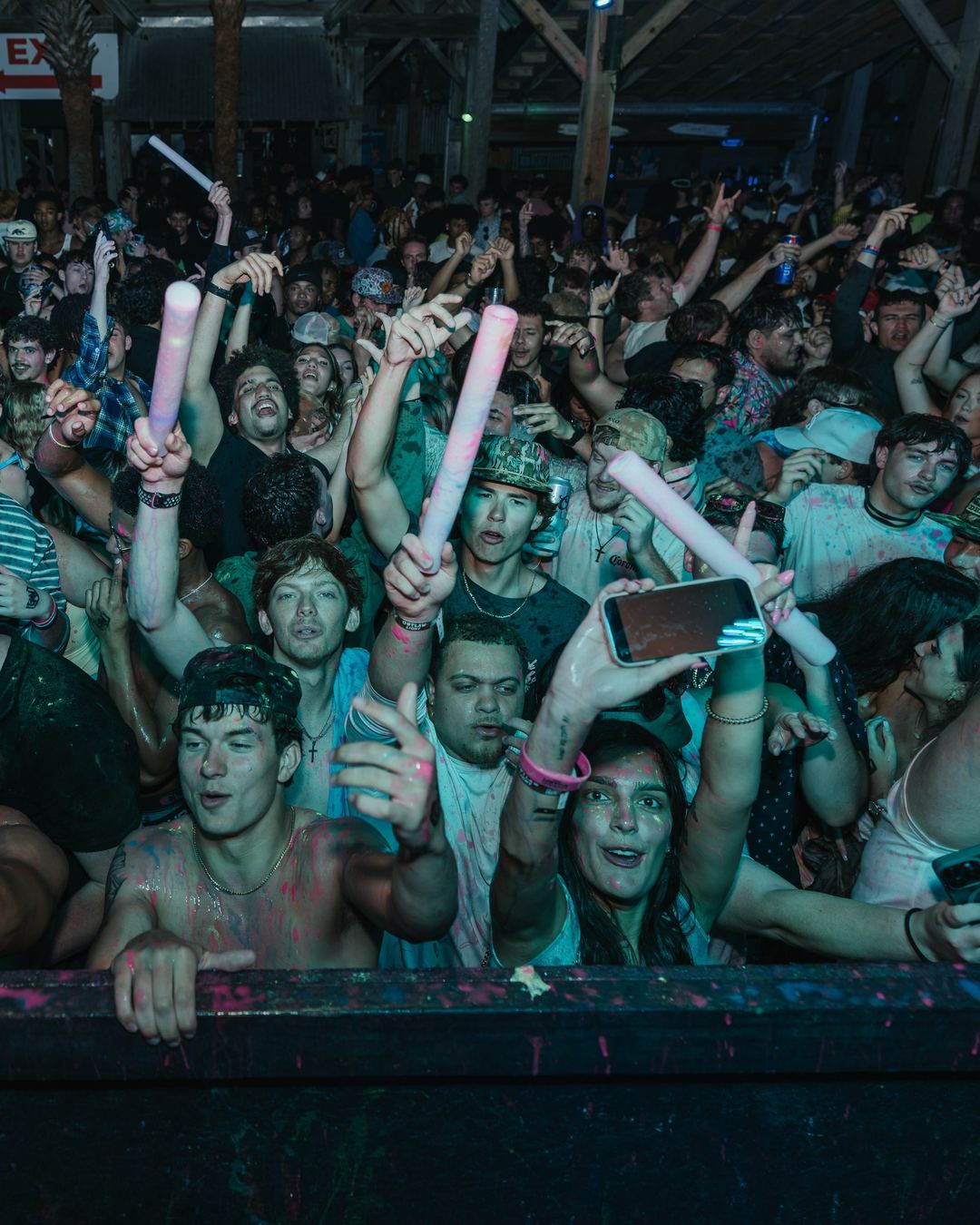 A spring break crowd with glow sticks and pink confetti in the air