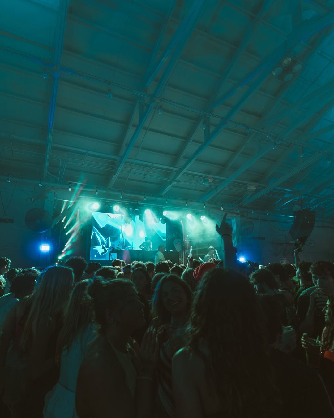 Teal stage lights over a spring break crowd inside an open-air club